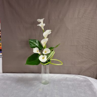 Arrangement de fleurs blanches avec des feuilles vertes dans un vase transparent.