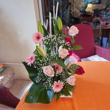 Arrangement de fleurs comprenant des roses, des lys, et des gerberas sur une table orange.