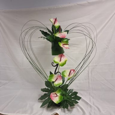 Arrangement de fleurs en forme de cœur avec des arums et des feuilles vertes.