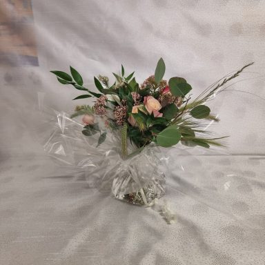 Un bouquet de fleurs variées dans un vase transparent avec un fond neutre.