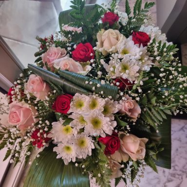 Bouquet de roses et fleurs blanches avec feuillage vibrant, sur une surface claire.