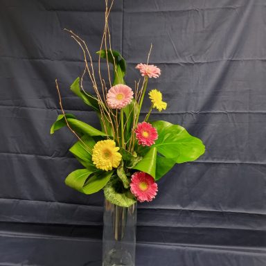Arrangement de fleurs colorées avec des feuilles vertes dans un vase transparent.