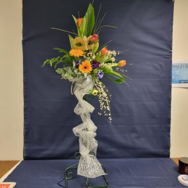 Arrangement de fleurs colorées avec un ruban décoratif sur un fond bleu.