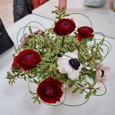 Bouquet coloré avec des roses rouges, anémones blanches et verdure en spirale.