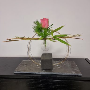 Composition florale minimaliste avec une rose pink sur un support en pierre.