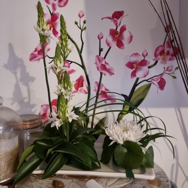 Arrangement de fleurs blanches et roses dans un pot, avec des éléments décoratifs.