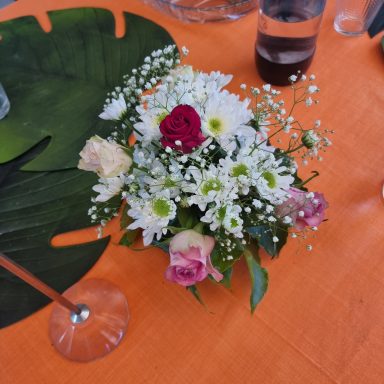 Bouquet de fleurs variées, comprenant des roses et des marguerites, sur une nappe orange.